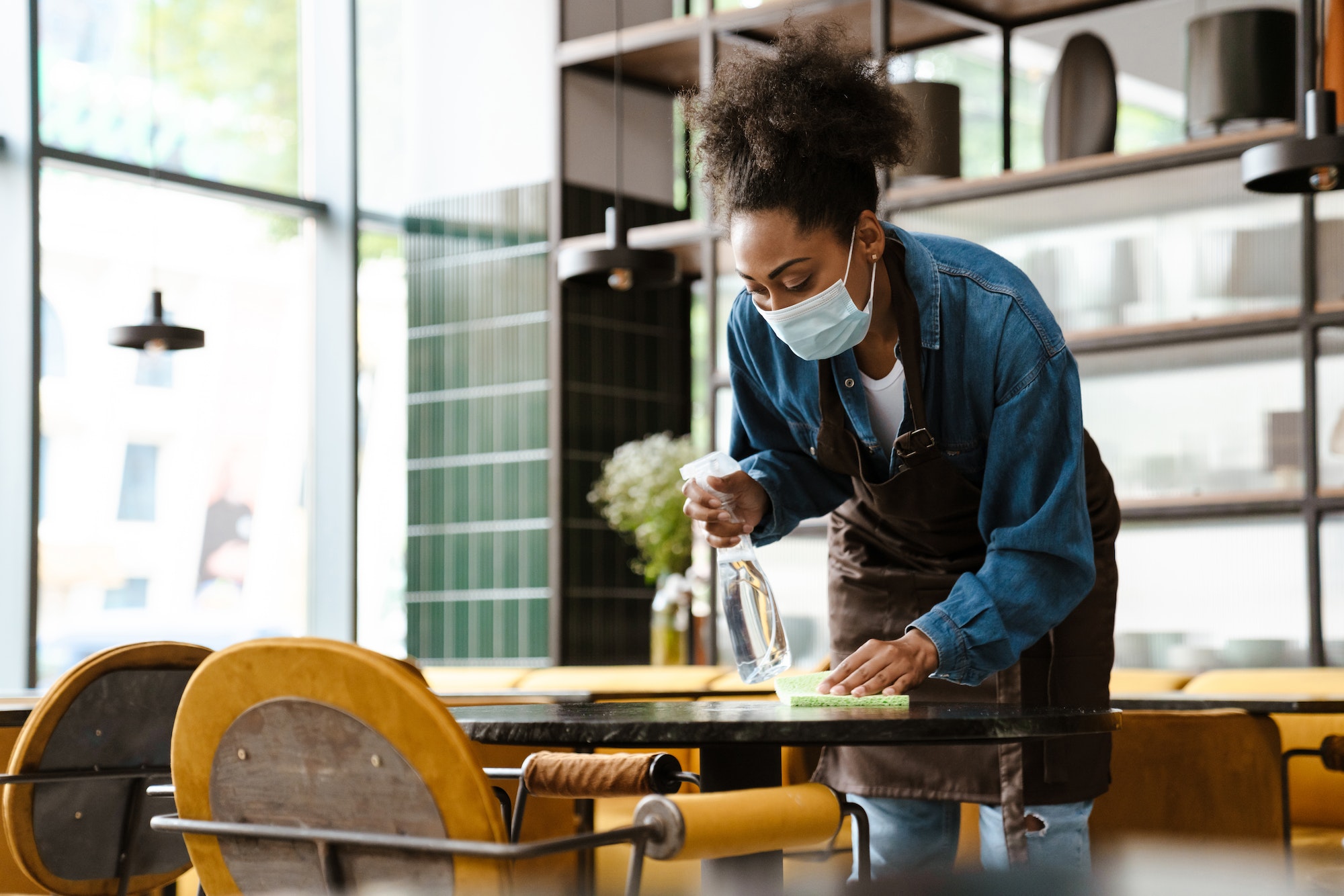 Black waitress wearing apron cleaning table while working in cafe