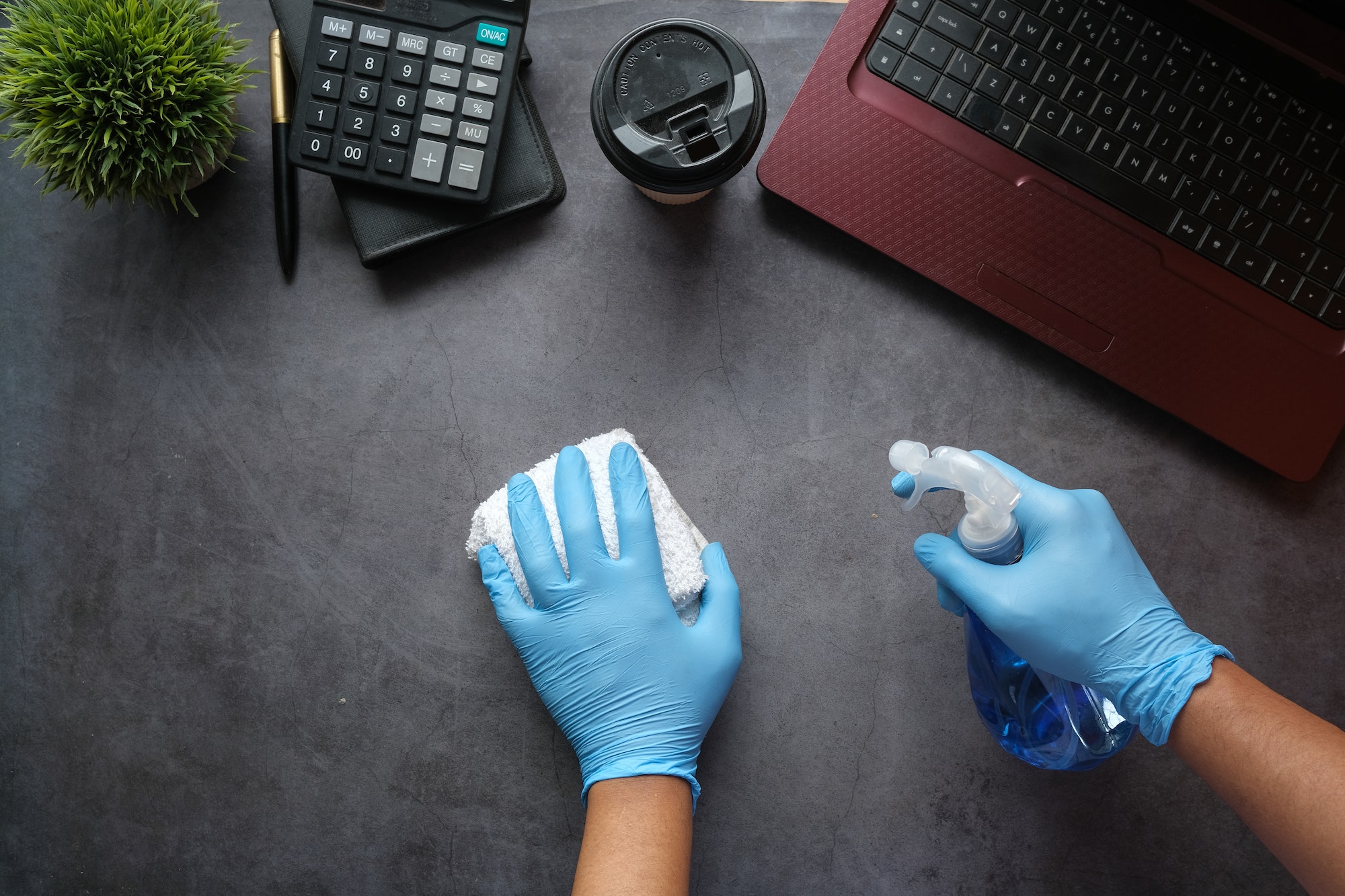 hand in blue rubber gloves holding spray bottle cleaning office table